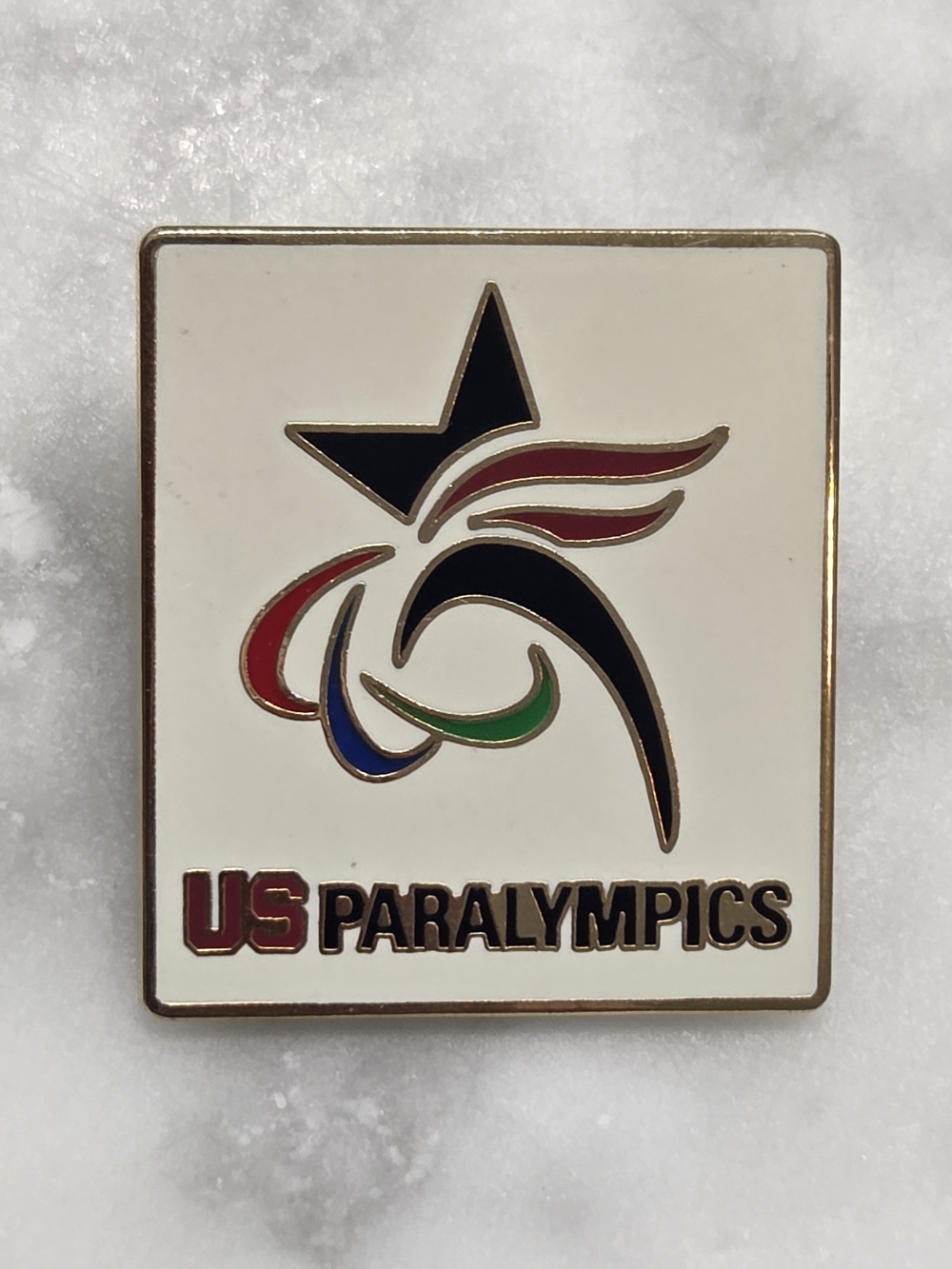 Team USA accessory is a square white enamel pin featuring the U.S. Paralympics